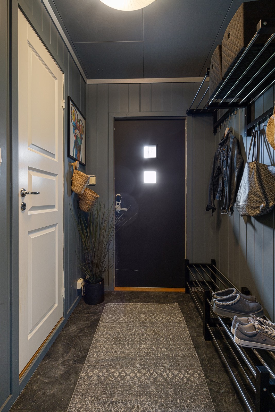 Entréen i hoveddelen har flismønstret laminatgulv - mens tak og vegger er malt i en mørk gråtone. Deler av rommet har åpen garderobeløsning. Galleribilde