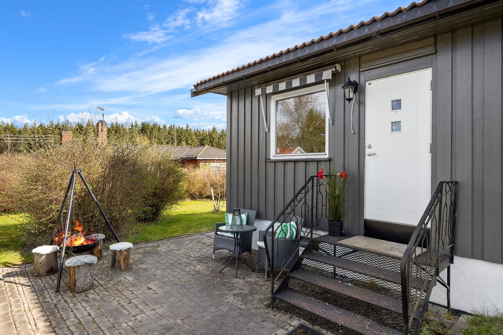Inngangen til hybeldelen ligger skjermet til på motsatt side av hoveddelens inngangsparti. Her er det etablert en hyggelig uteplass med bålpanne og plass til enkelt utemøblement. Galleribilde