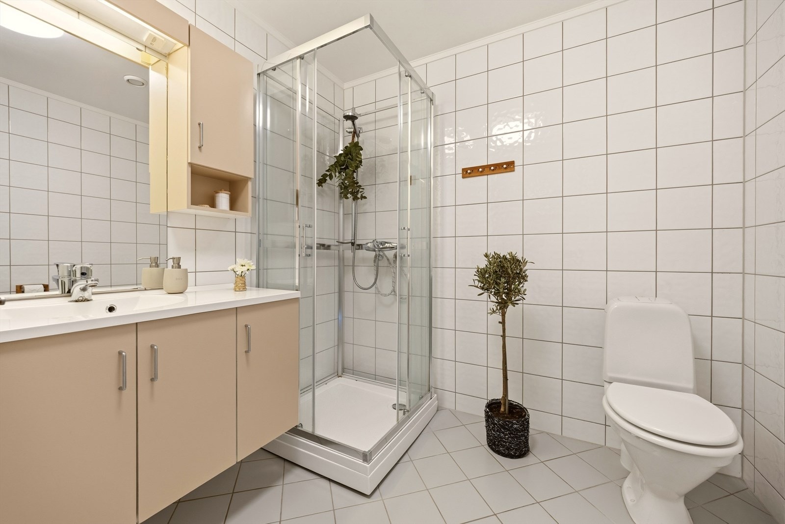 Badet er utstyrt med heldekkende servant med underskap, speil, veggskap, dusjkabinett og toalett Galleribilde
