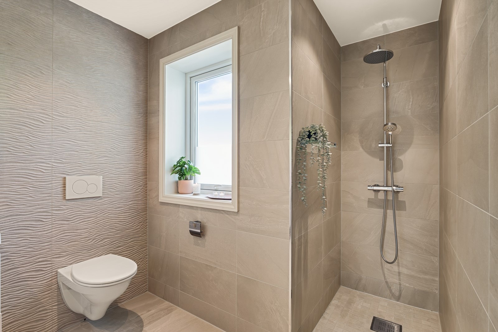 Her er det laget til en egen dusjnisje og flotte flisevalg. Badet er ellers innredet med vegghengt toalett, servant med møblement og speil. Galleribilde