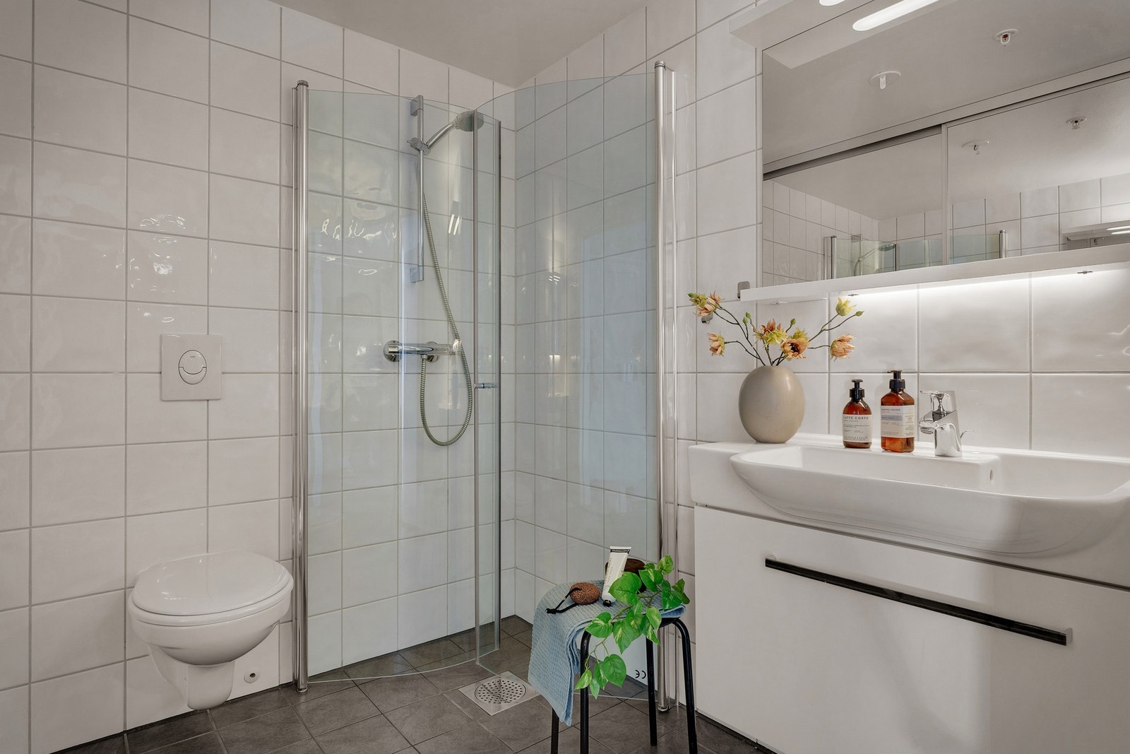 - Badet er lyst og trivelig, med flislagte overflater og praktisk innredning med dusjdører i glass, vegghengt toalett og opplegg for vaskemaskin - Galleribilde