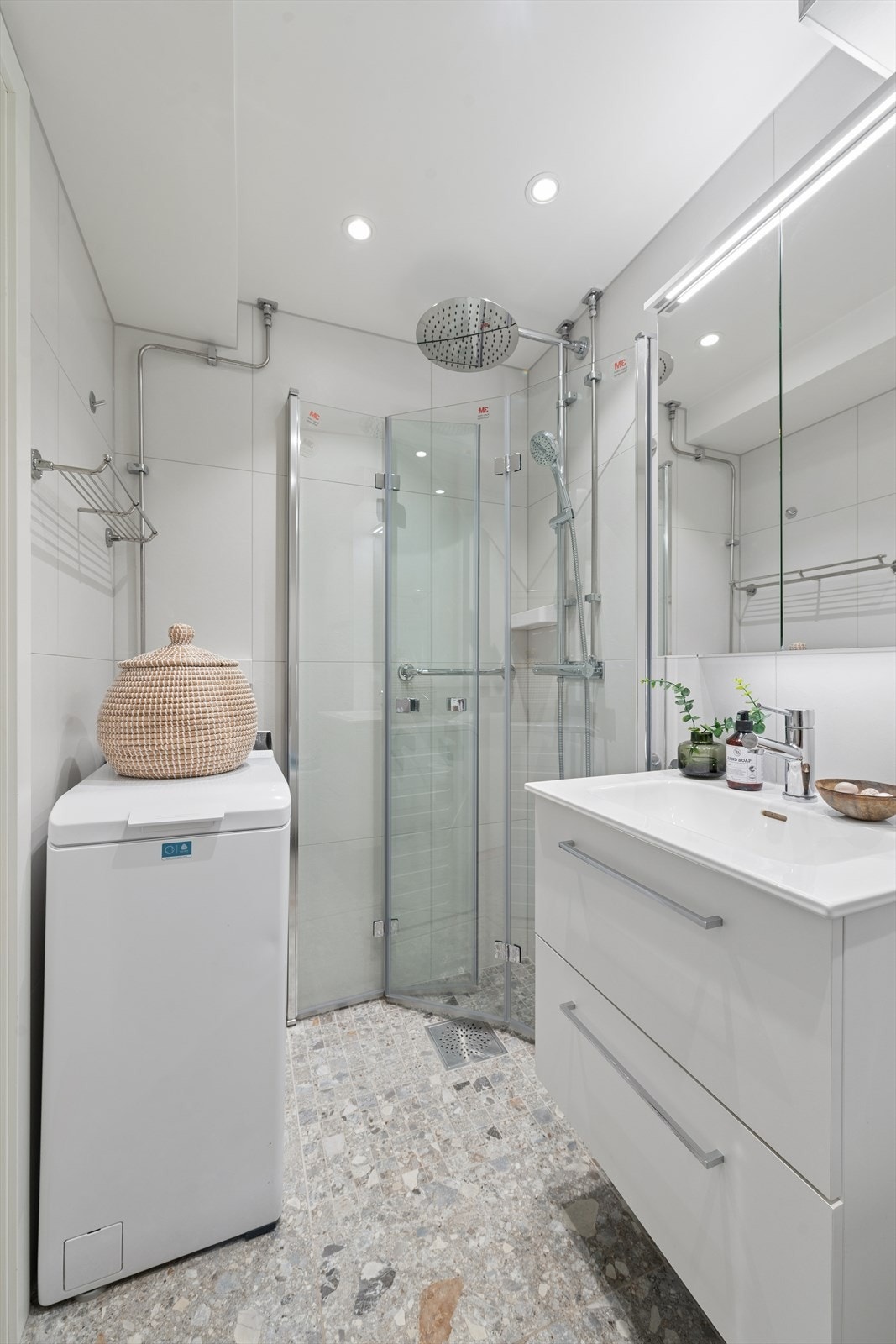 Badet er utstyrt med nedfelt servant i servantmøbel, speilskap med belysning, veggmontert toalett, dusjhjørne og vaskemaskin som medfølger salget. Det er gjort ekstra tilvalg på badet for ca. kr. 100 000,-. Galleribilde