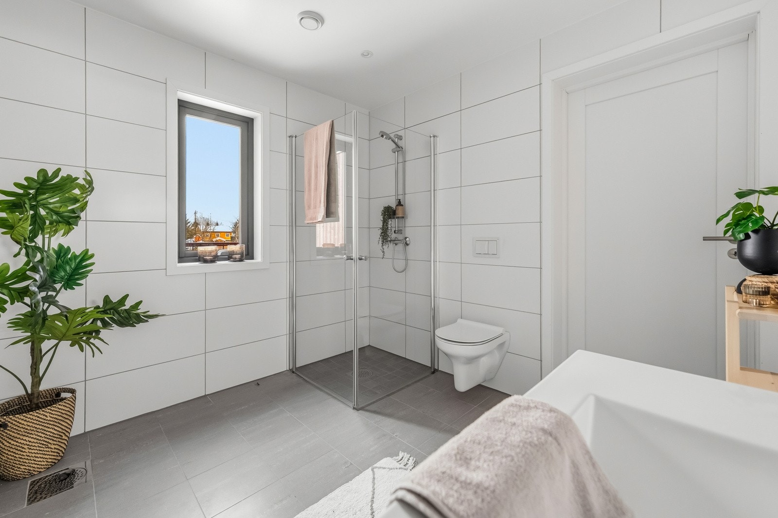 Gulv: Grå standardflis 30x30 cm med varmekabler (10x10 cm i dusjsonen i samme farge). Vegger: Matt hvit flis 30x60 cm. Badet er påkostet utover opprinnelig standard og leveres med badekar. Galleribilde