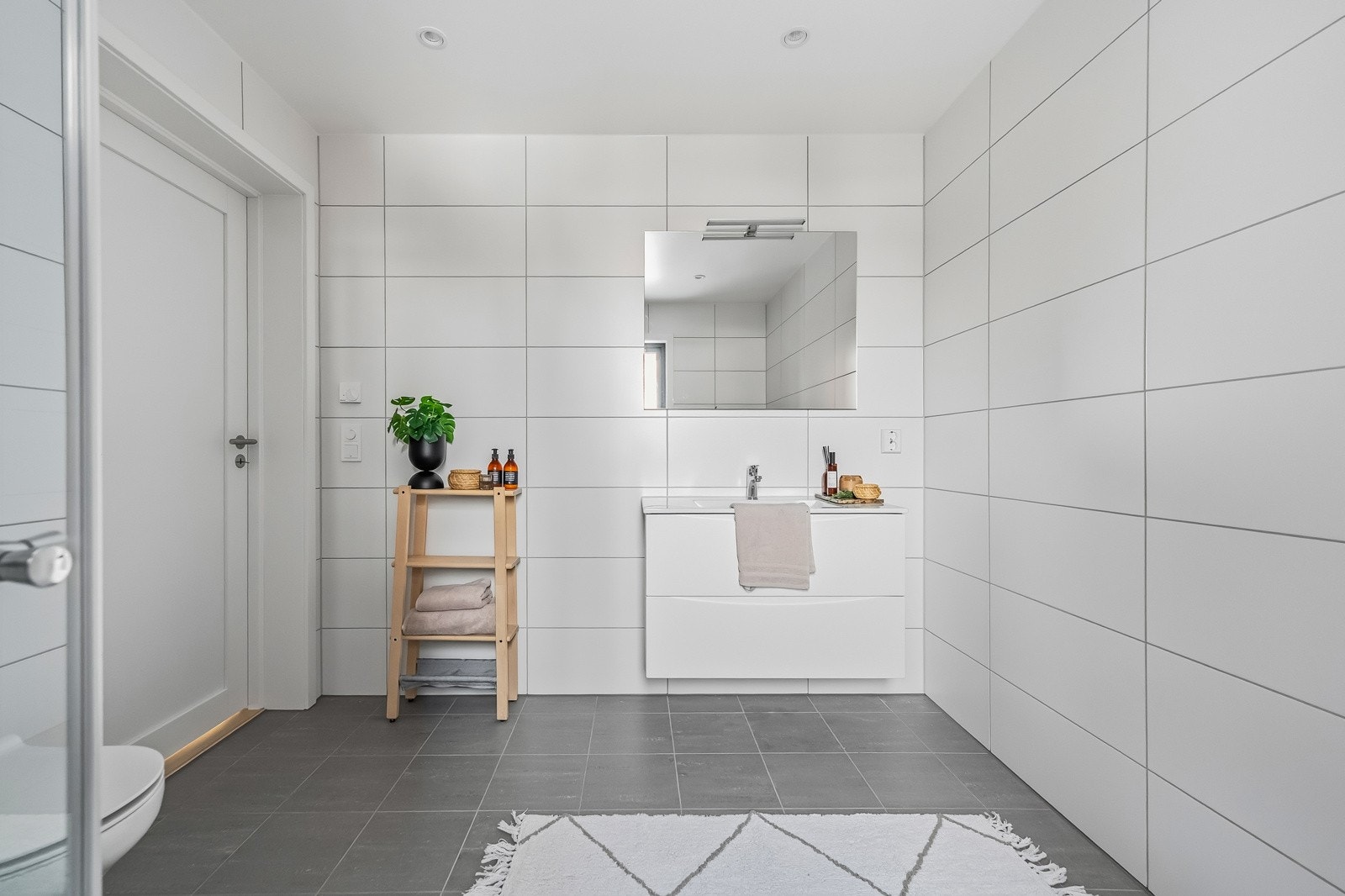 Det romslige hovedbadet ligger praktisk til i nærhet av soverommene og får en moderne og tidløs finish. Baderomsinnredningen leveres med hvite fronter, skuffer, heldekkende servanttopp og speil. Galleribilde
