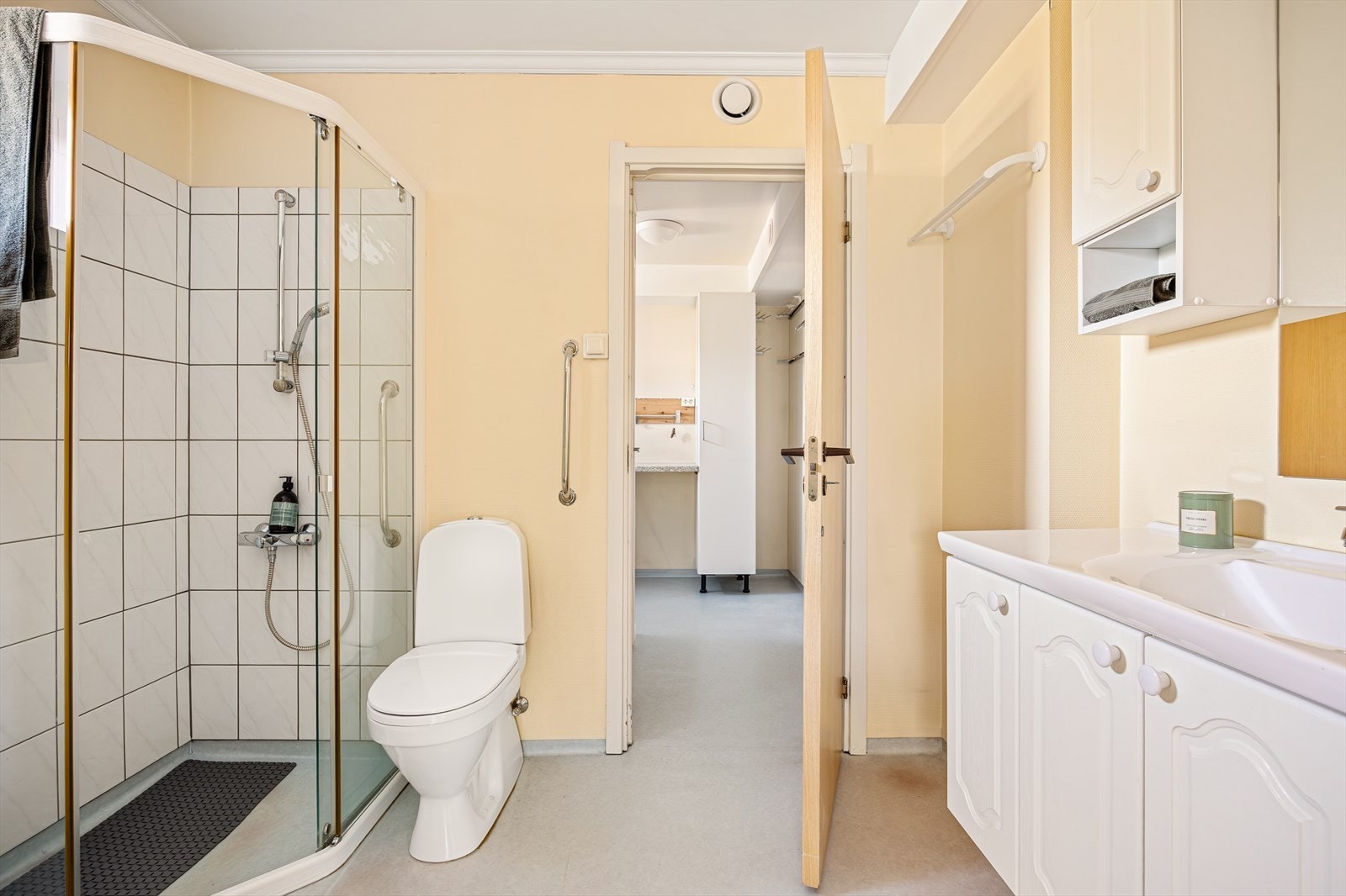 Badet er innredet med dusjløsning, servant og wc. Overflater består av belegg på gulv, malt strie på vegger og fliser i dusjkrok. Galleribilde