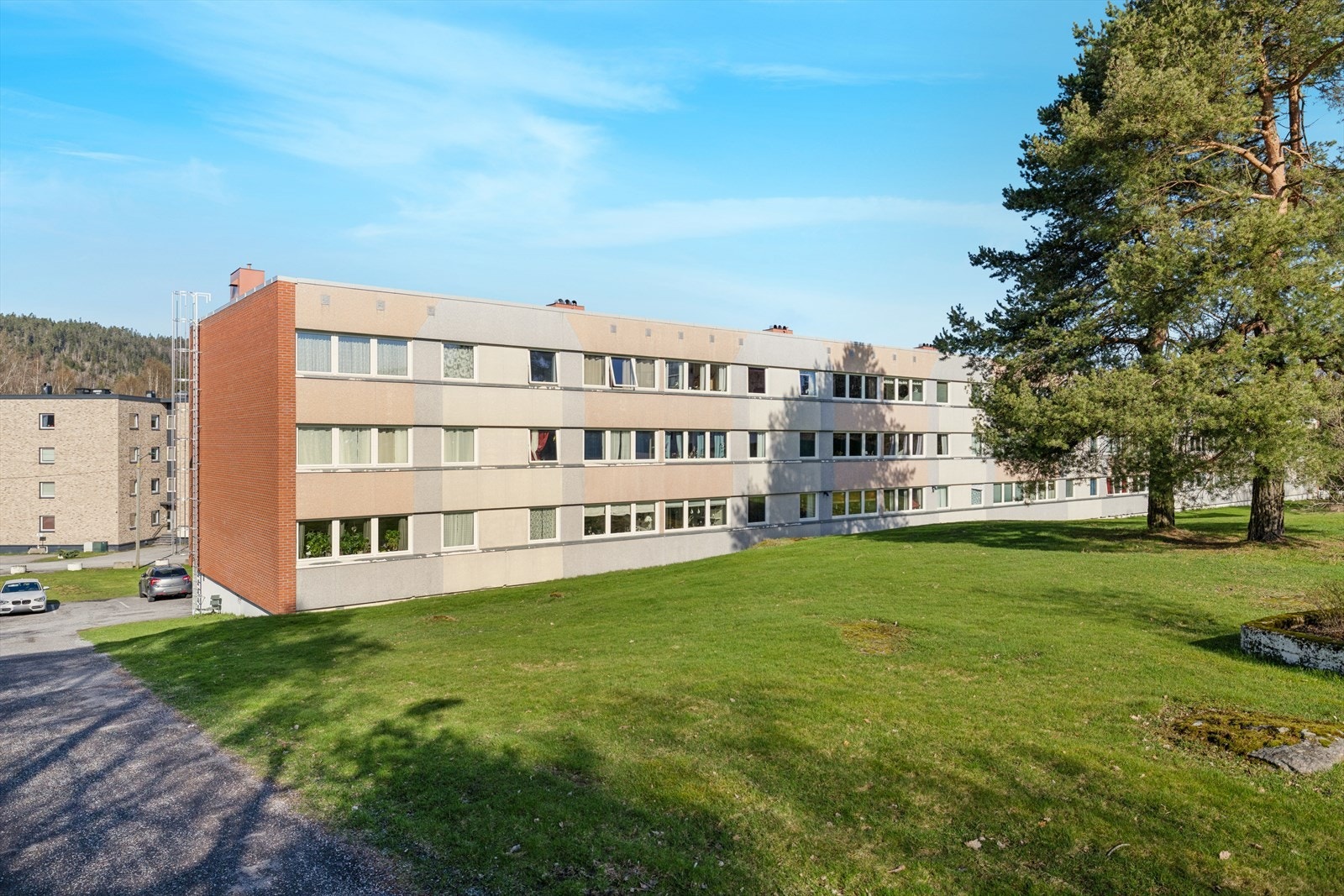 Fasade av borettslaget med godt vedlikeholdte fellesområder og parkering rett utenfor. Galleribilde