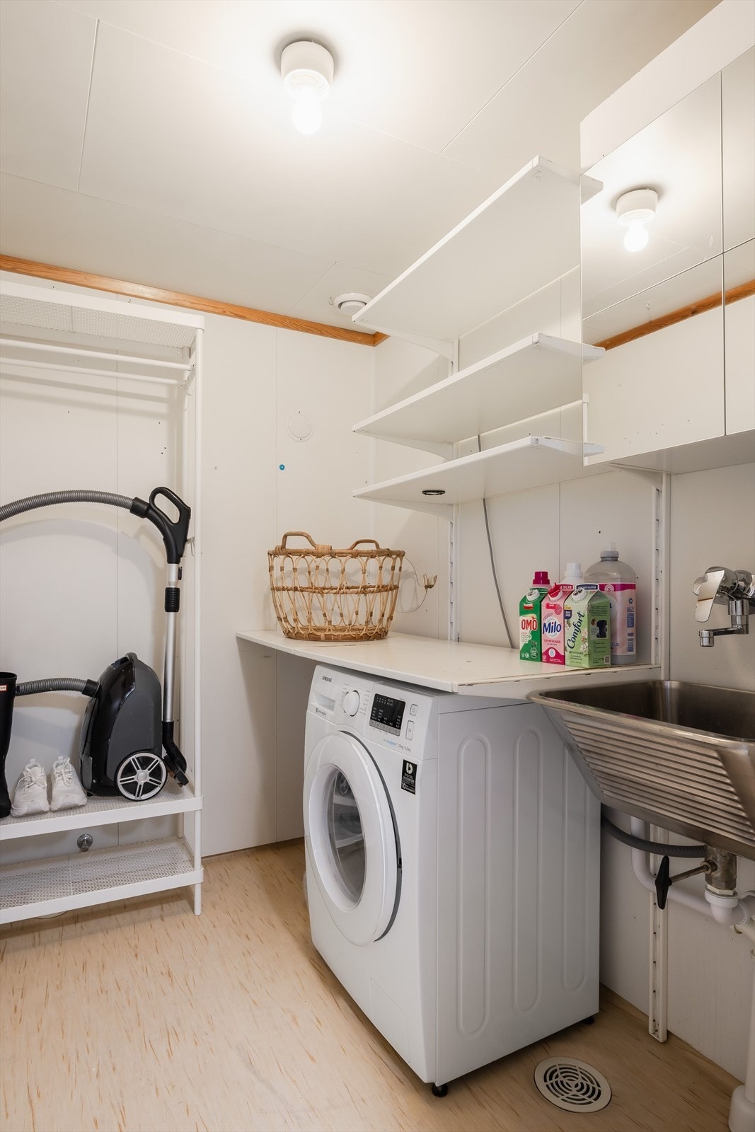 Praktisk vaskerom med utslagsvask, opplegg for vaskemaskin og diverse hyller og skap for oppbevaring. Galleribilde