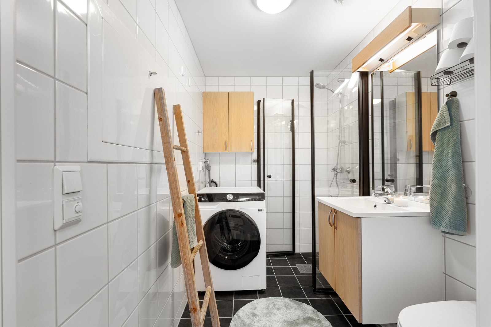 Moderne flislagt bad utstyrt med kran og avløp for vaskemaskin. Galleribilde