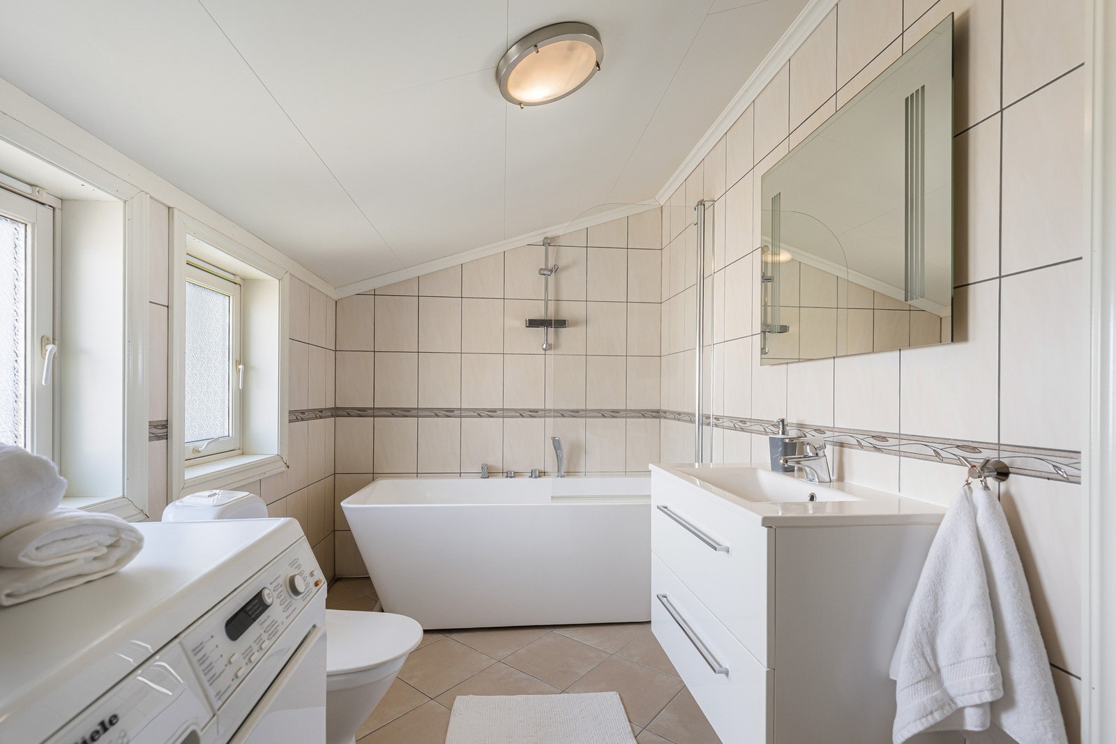 Flislagt bad med badekar, opplegg for vaskemaskin og praktisk innredning. Galleribilde