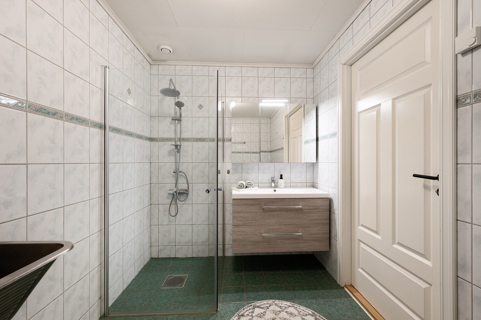 Badet er utstyrt med dusjhjørne med dører i herdet glass og baderomsinnredning med servant. Galleribilde