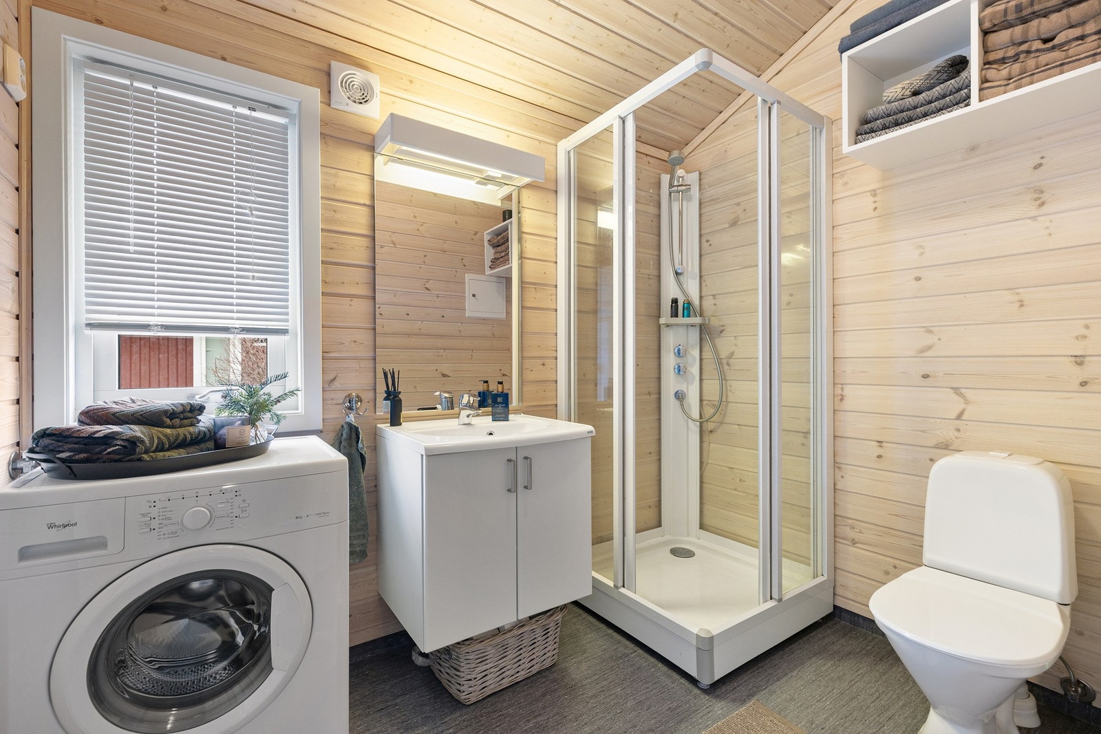 Badet har belegg på gulv og panel på vegger og i himling. Rommet er utstyrt med toalett, servant med innredning, dusjkabinett og opplegg for vaskemaskin. Galleribilde