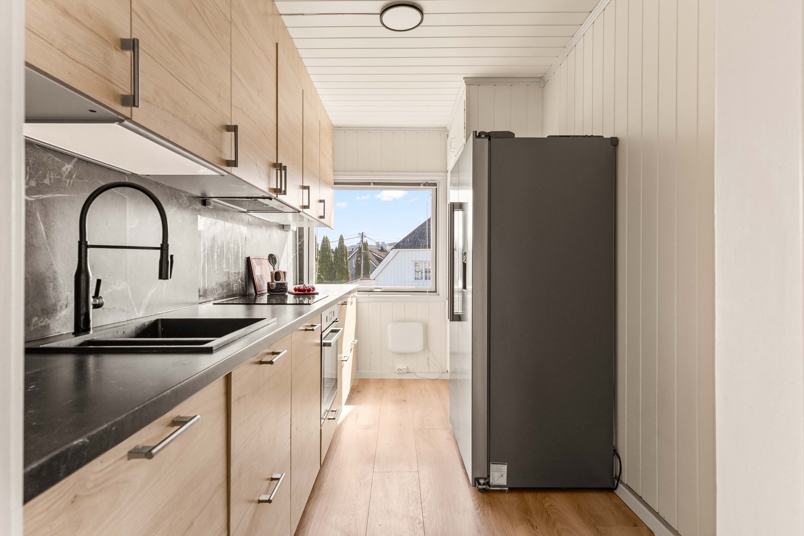 Kjøkkenet i andre etasje, fra IKEA, har glatte, folierte fronter, laminat benkeplate med nedfelt kum i kompositt og flislignende plater over benkeplaten. Galleribilde
