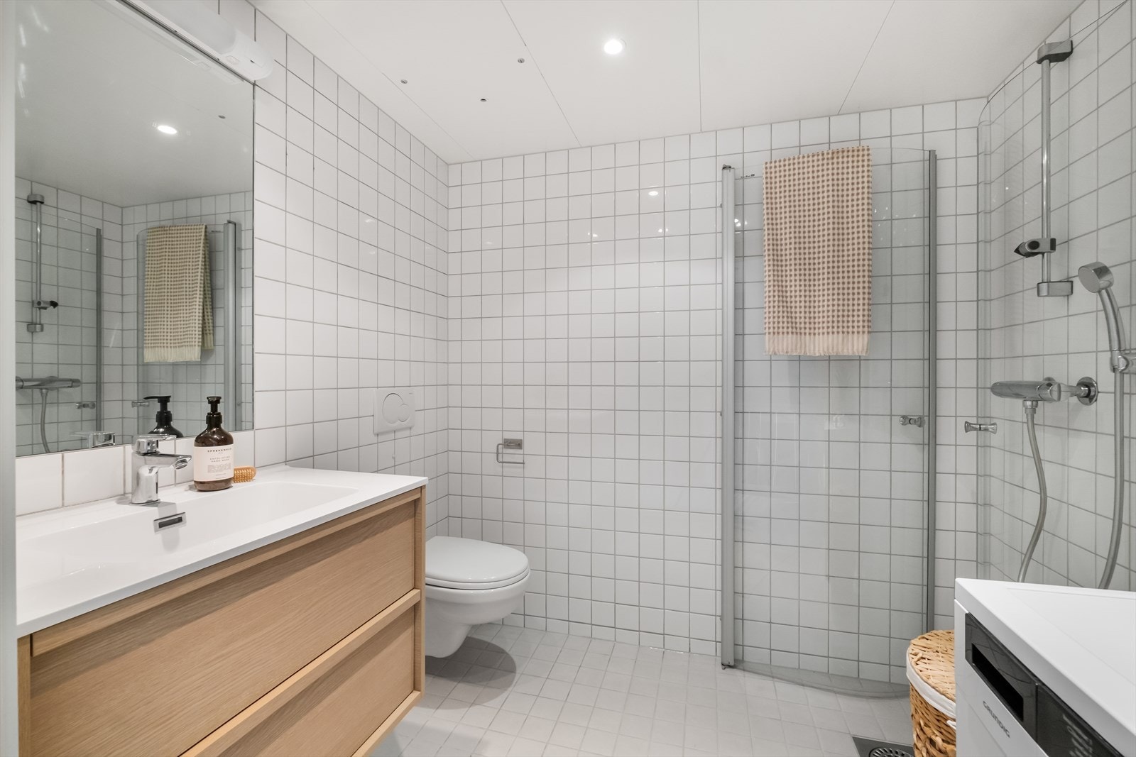 Badet er innredet med dusjhjørne med glassdører, vegghengt toalett, opplegg for vaskemaskin og plass til tørketrommel. Galleribilde