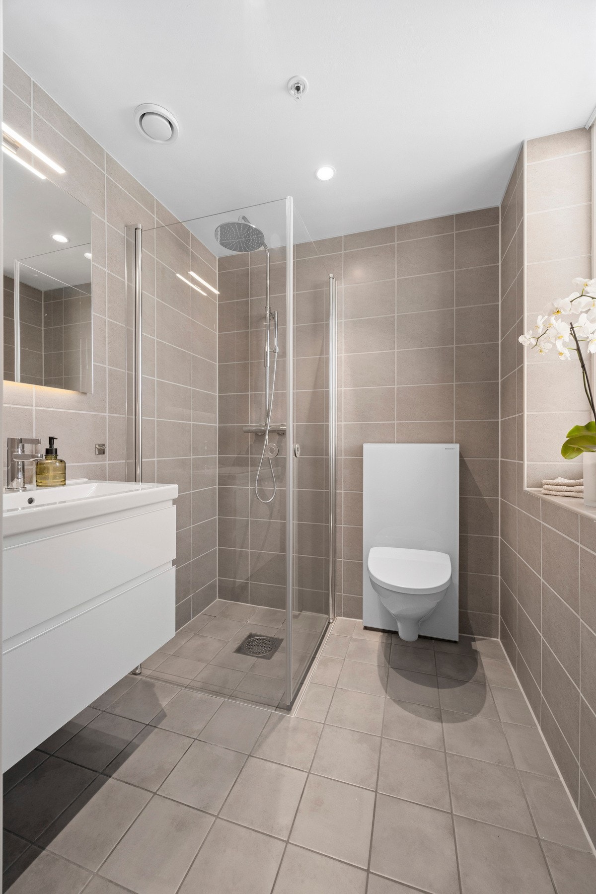 Delikat og tiltalende bad i direkte tilknytning til hovedsoverommet. Badet er utstyrt med vegghengt toalett, servant og dusjhjørne med dører av glass og regnfallsdusj. Galleribilde