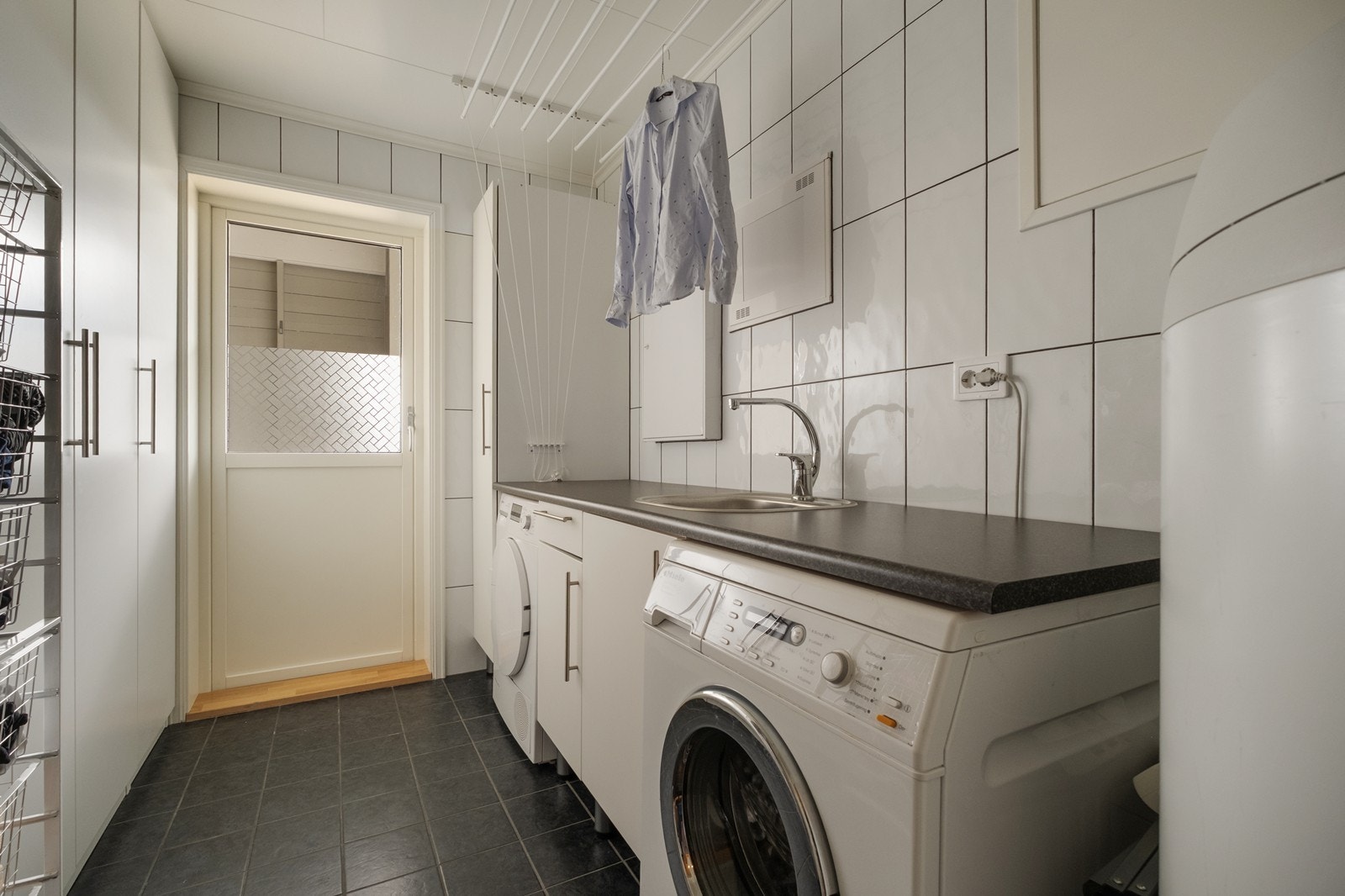 Fra badet har man direkte tilgang til flislagt og praktisk innredet vaskerom, som også har dør ut til markterrasse. Galleribilde