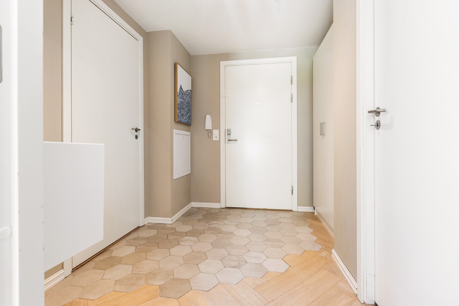 Stor entrè med garderobeskap og tilgang til bad og ekstra bod. Legg merke til gulvet som har en moderne kombinasjon av fliser og parkett. Galleribilde