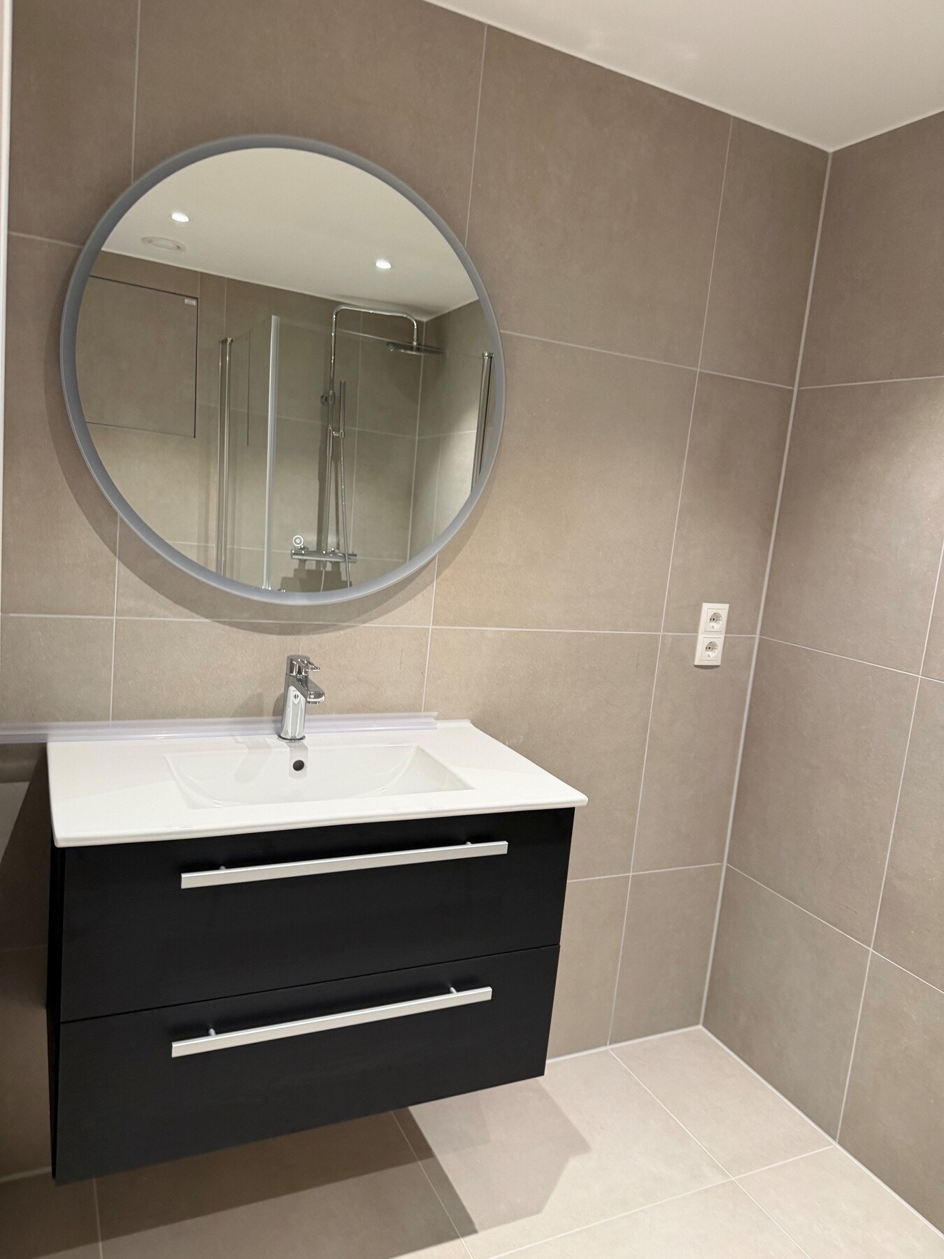 Badet får et moderne og gjennomført uttrykk med fliser i en lun beige tone på både gulv og vegger. Galleribilde