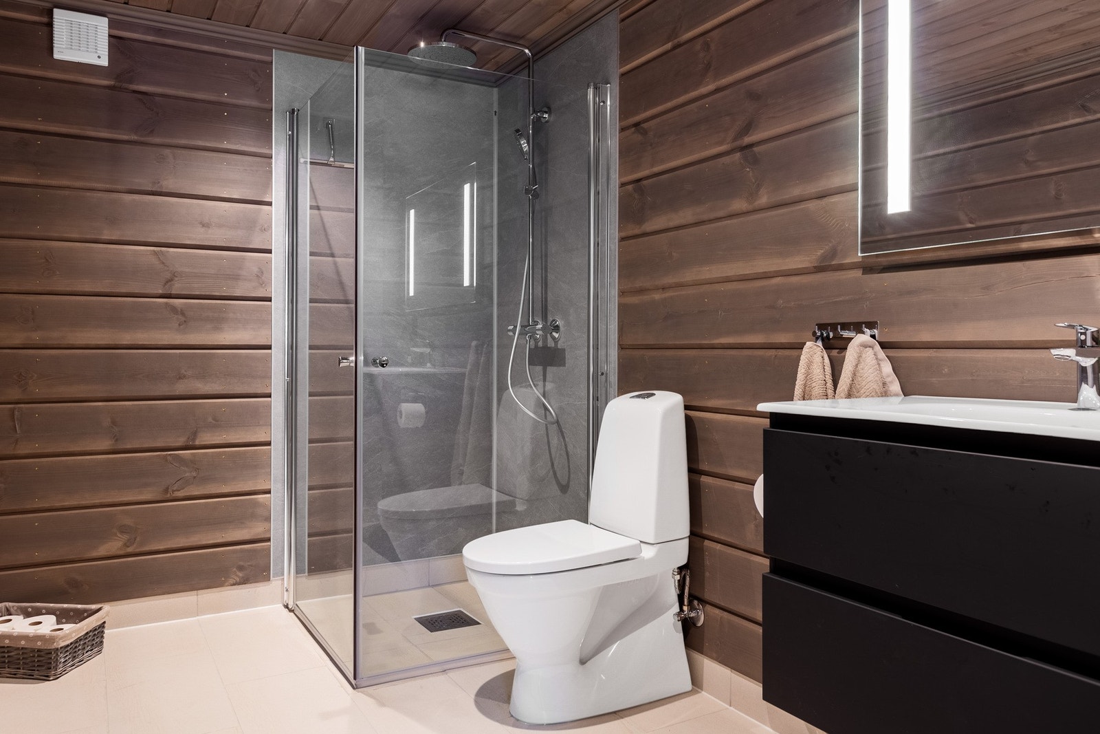 Badet har gulv belagt med flis med varmekabler, og vegger kledd i panel og flis i dusjsone. Innredet med baderomsinnredning med servant, speil, gulvmontert toalett og dusjhjørnet. Galleribilde