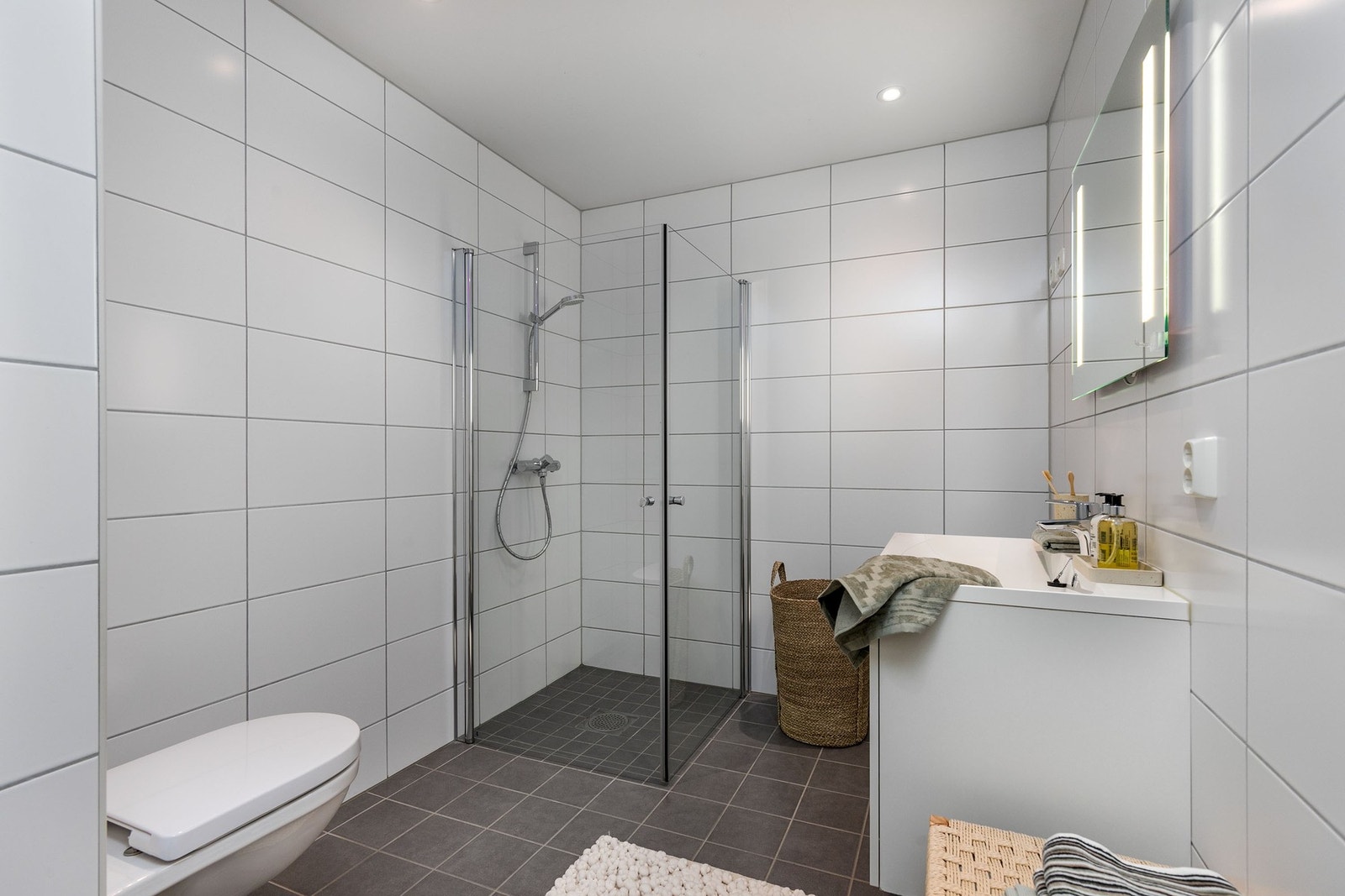 Badet er utstyrt med servantmøblement, speil med integrert belysning, vegghengt toalett og dusjhjørne med innfellbare glassdører. Galleribilde