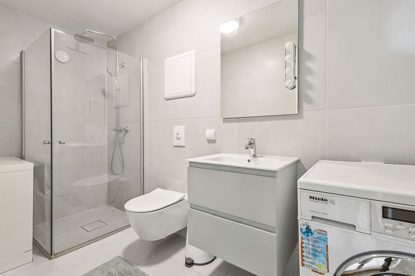 Lyst og pent flislagt bad med varmekabler i gulvet. Dette badet er også utstyrt med dusjhjørne med innfellbare glassvegger, vegghengt wc, servantinnredning med skuffer, samt opplegg og plass til vaskemaskin Galleribilde