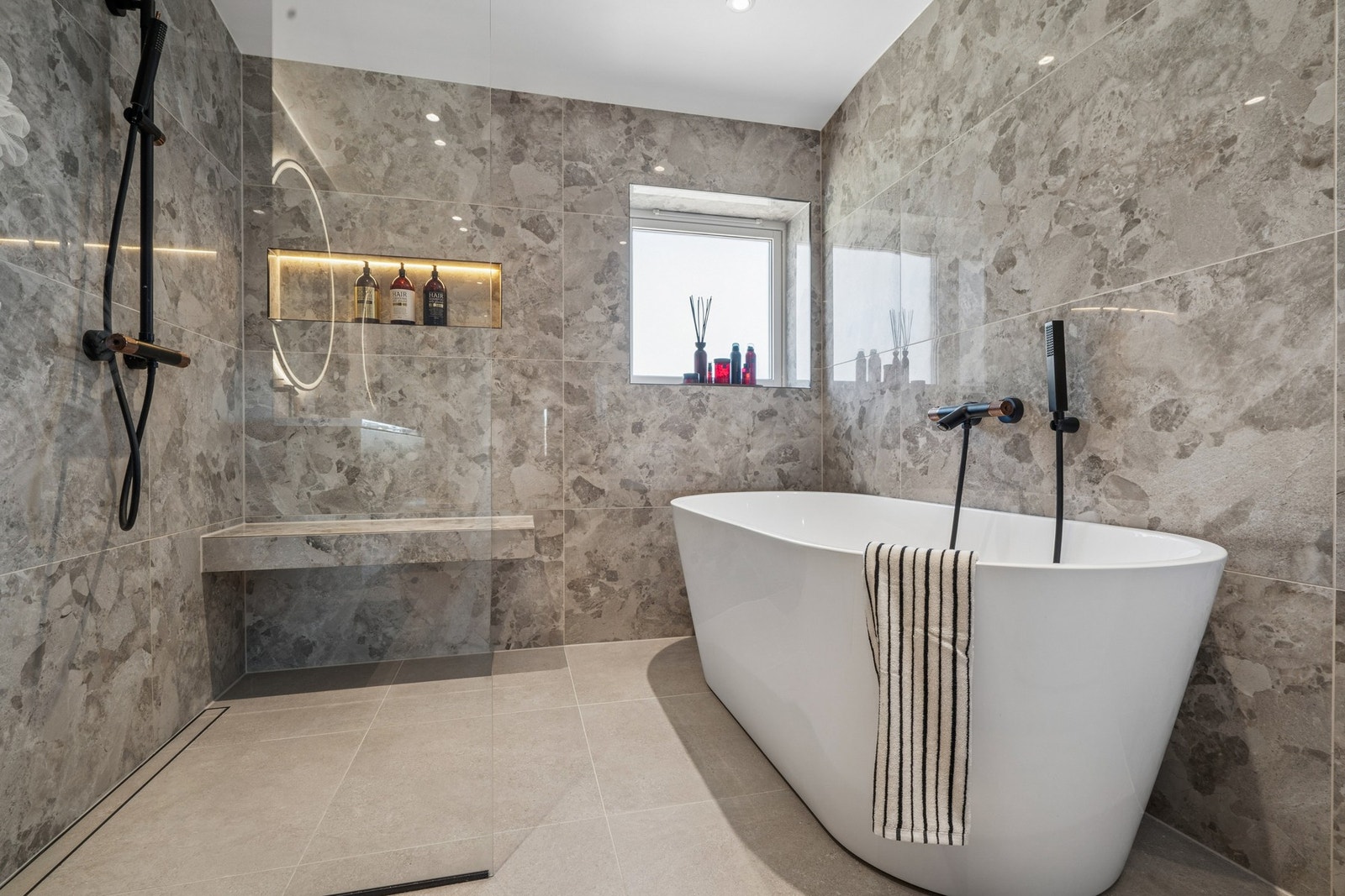 Badet holder en god størrelse og er utstyrt med både dusj og frittstående badekar. Dusjsonen har sittebenk og praktisk nisje med integrert LED-belysning. Galleribilde