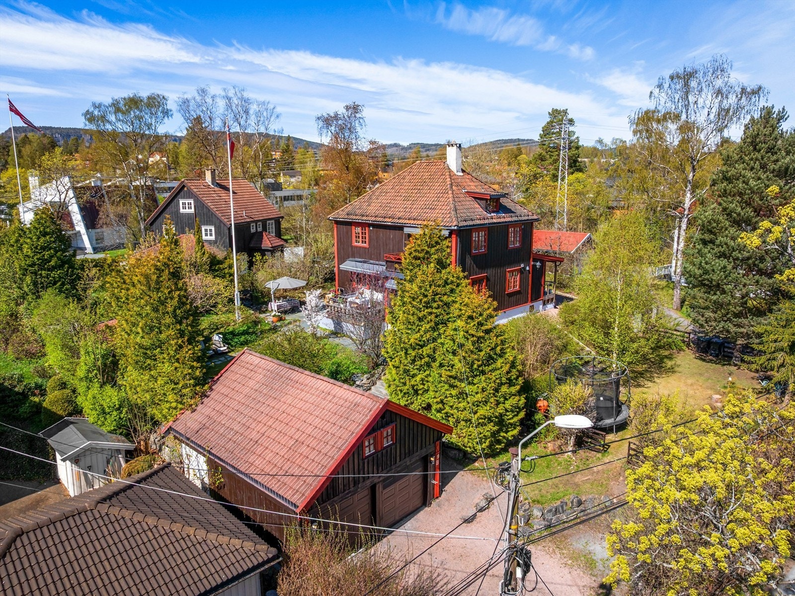 Oversikt over eiendommen med hovedhus, garasjer og den parkmessige hagen. Galleribilde