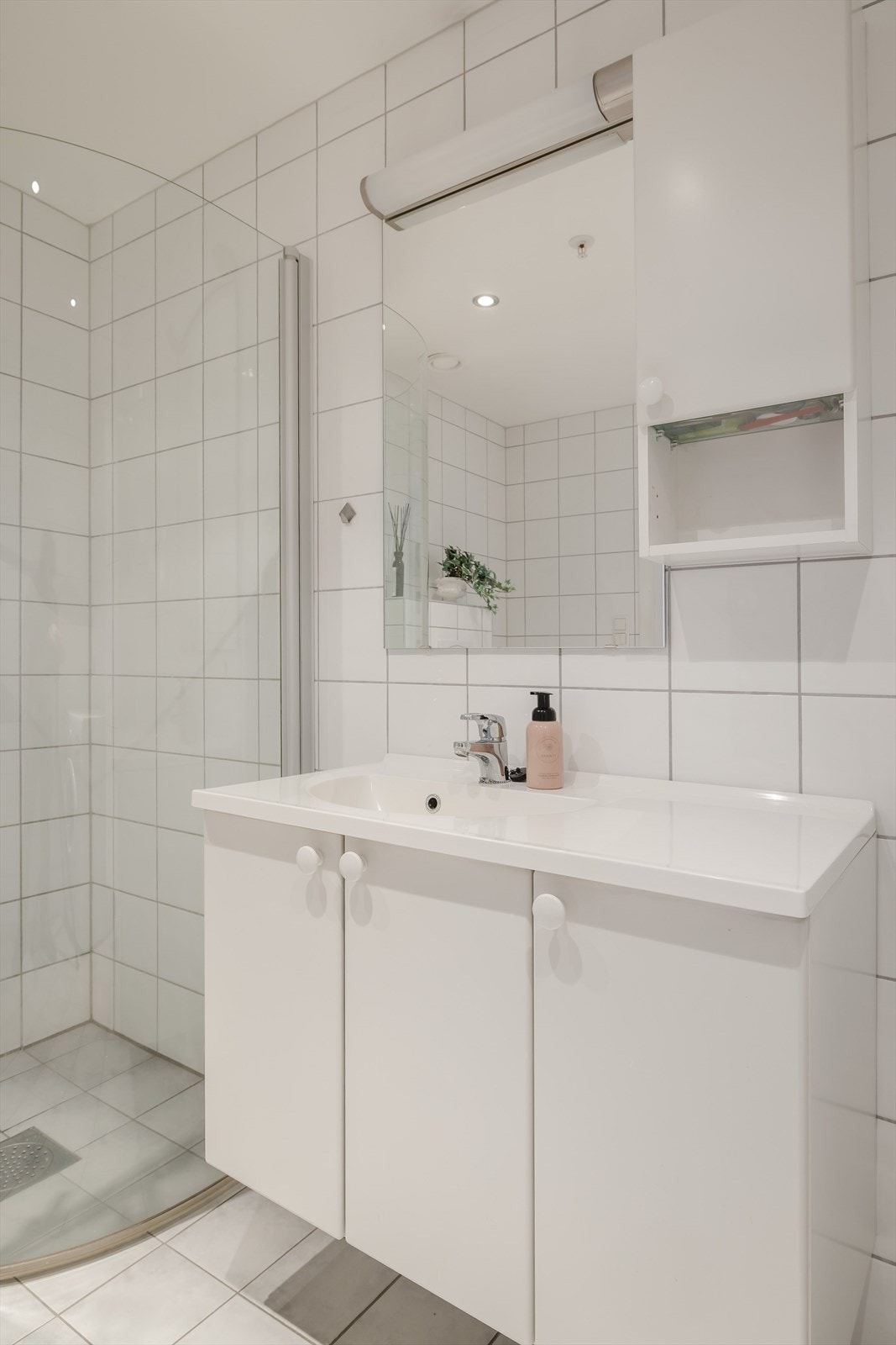 Baderomsinnredning med underskap og heldekkende servant. I overkant er det veggskap, speil og lys med elektrisk uttak. Galleribilde