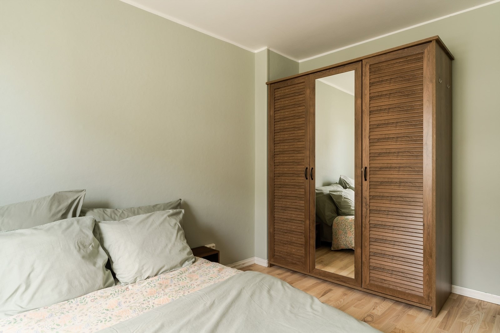 Det store vinduet gir godt med lys, og rommet oppleves som lunt og komfortabelt. En stilren garderobe med speilflate gir både praktisk lagring og en stilren look på soverommet. Galleribilde