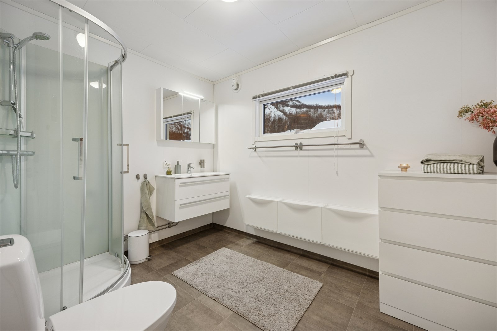 Badet er innredet med speil, servant med seksjon, toalett og dusjkabinett. Galleribilde
