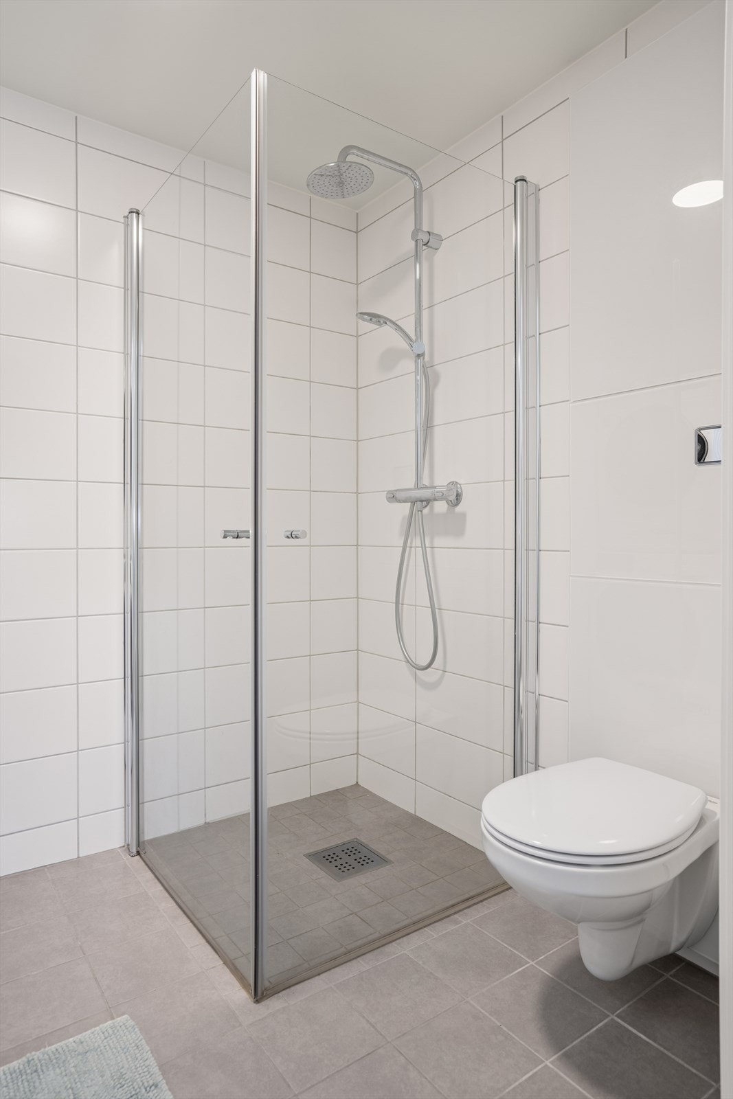 Badet er helfliset og utstyrt med vegghengt toalett og dusjhjørne med innfellbare glassdører. Galleribilde