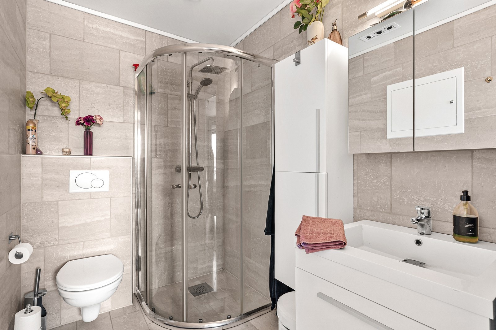 Badet er flislagt og er utstyrt med vegghengt toalett, dusjsone med glassdører, servant og speilskap. Galleribilde