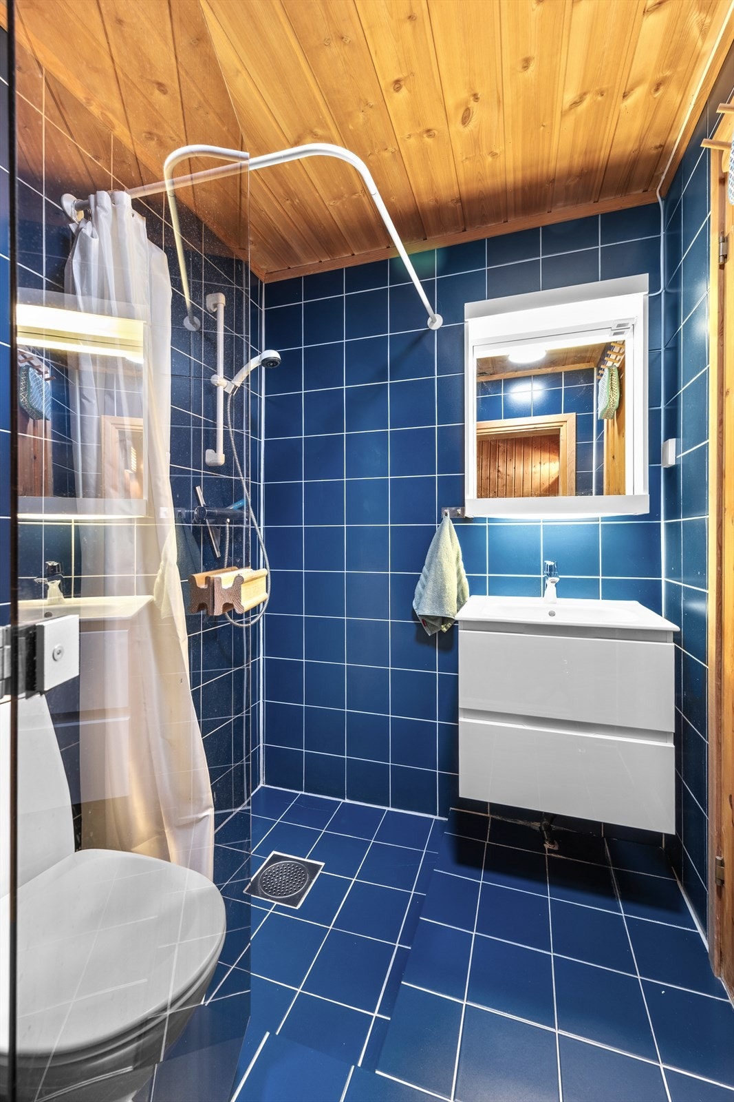 Det andre badet i underetasjen er også fra byggeår. Badet har flislagte overflater, mekanisk ventilasjon, heldekkende servant på underskap, speil med belysning, klosett og dusj. Galleribilde