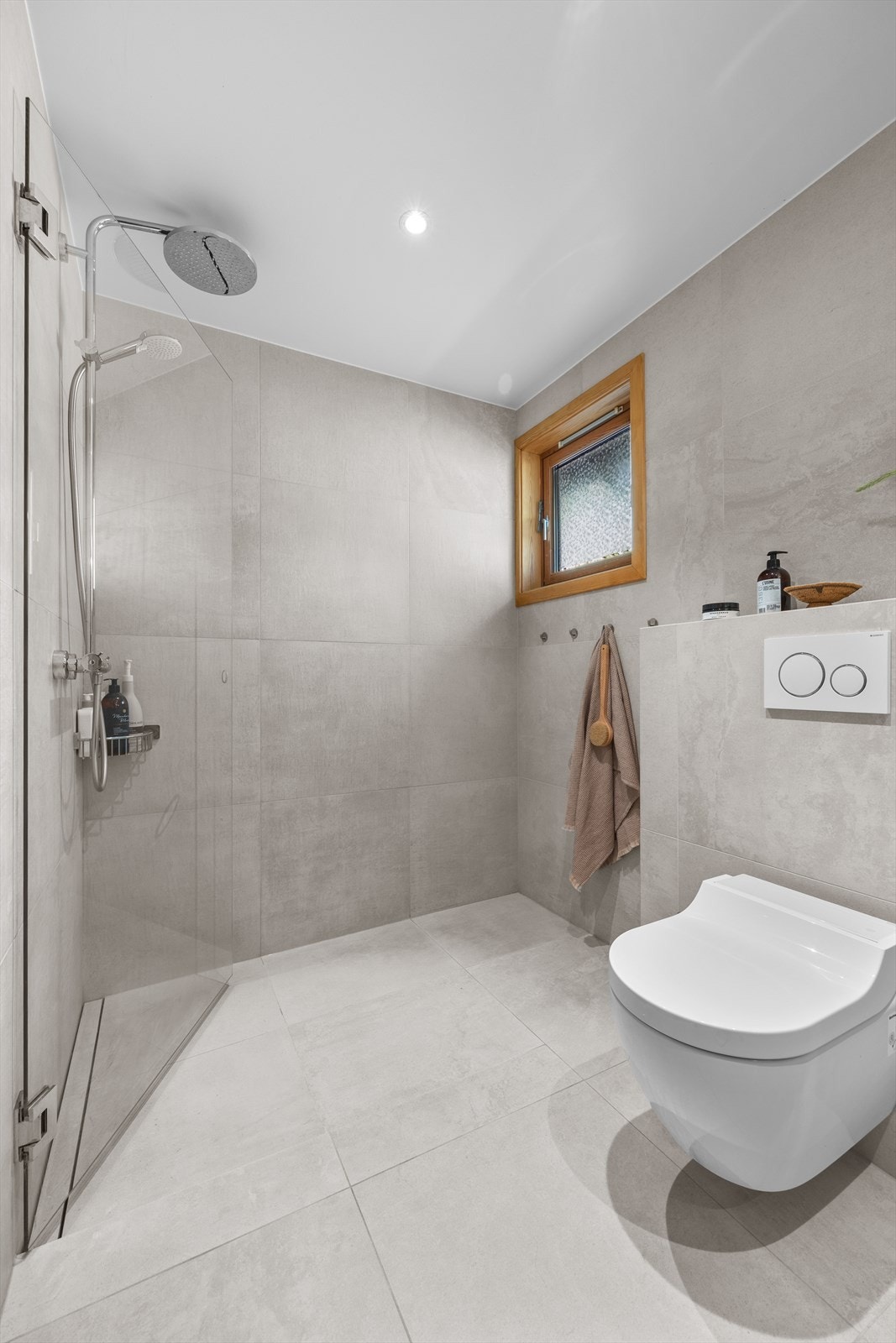 Badet er flislagt og har varmekabler i gulv, heldekkende servant på underskap, speil med belysning, vegghengt klosett og dusj med dusjvegger i herdet glass. Galleribilde