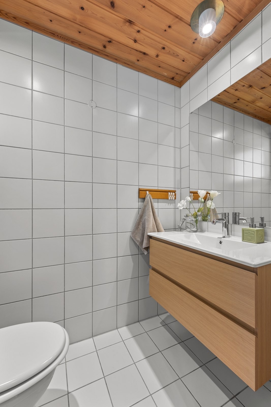 Praktisk gjeste-wc med flislagt gulv og vegger. Rommet er innredet med servant, speil og vegghengt klosett, og har mekanisk avtrekk. Galleribilde