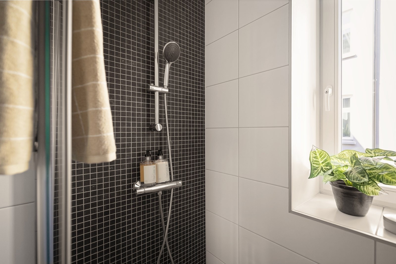 Dusjhjørne med skyvedør og mørke mosaikkfliser i dusjsonen. Badet har mekanisk avtrekk. Galleribilde