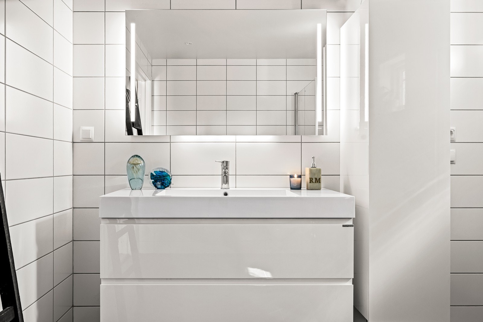 Baderomsinnredningen er stilren med heldekkende servant og lagringsplass i skuffene. Det er også montert høyskap i samme design. for ytterligere lagringsplass. Galleribilde