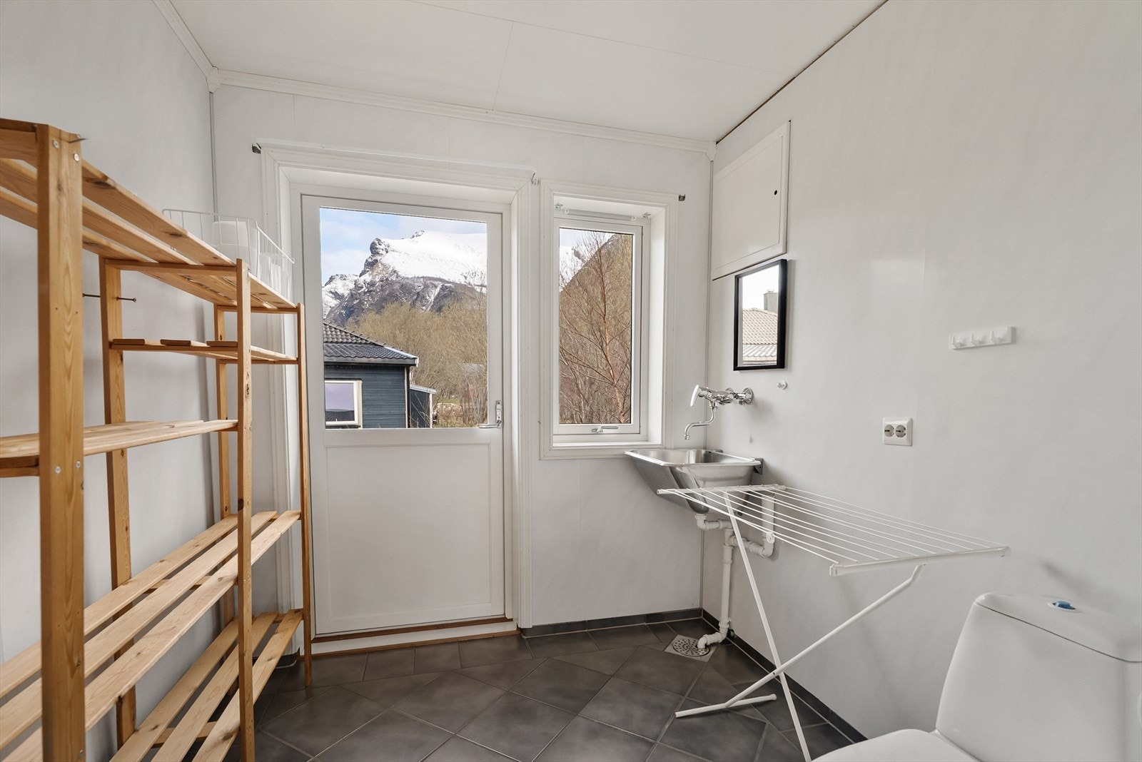 Praktisk vaskerom med flislagt gulv med varme utstyrt med toalett, opplegg for vaskemaskin og skyllekar på vegg. Galleribilde