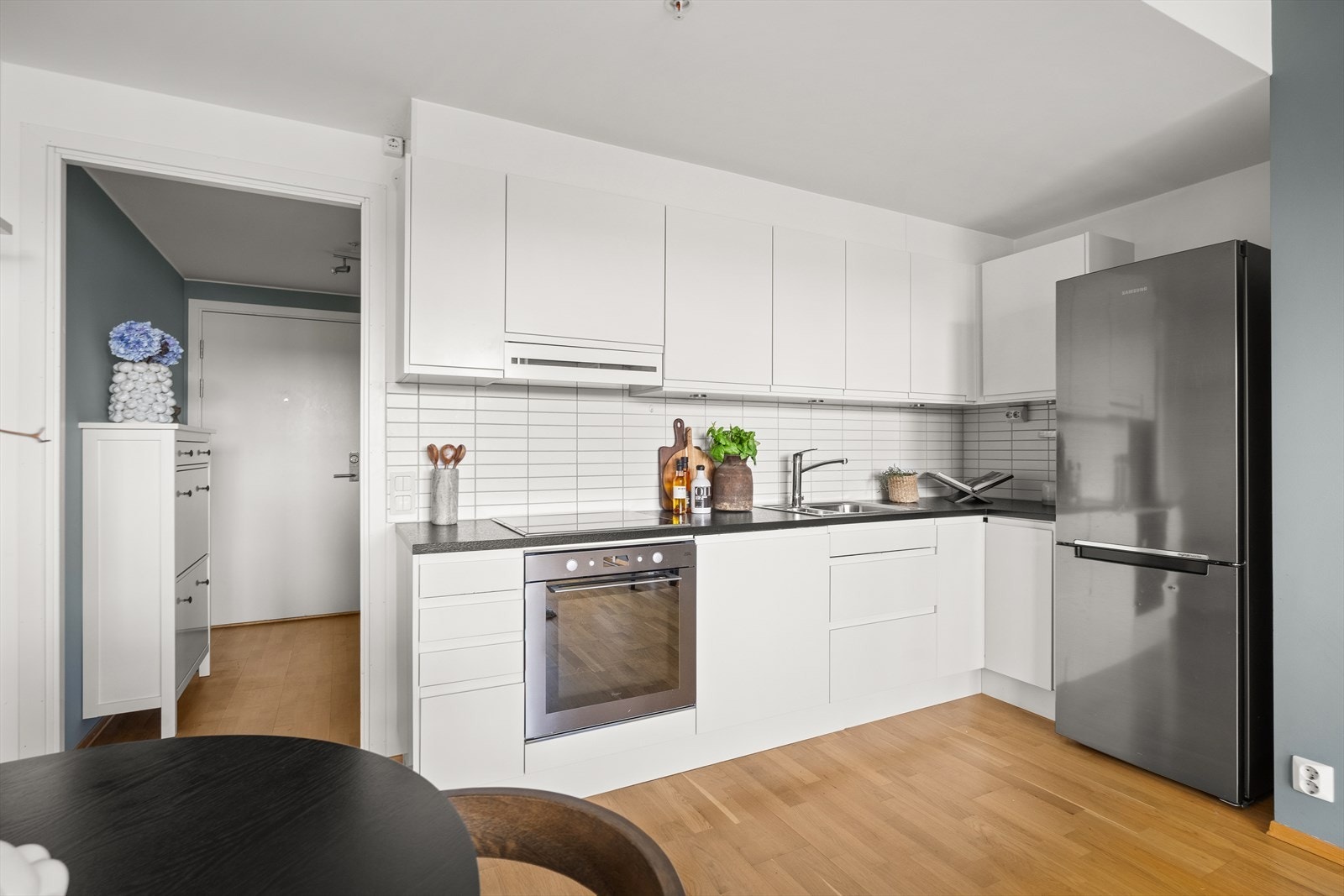 Lyst og moderne kjøkken i åpen løsning. Kjøkkeninnredning fra 2012 med glatte fronter, fliser på vegg over kjøkkenbenk og benkeplate i laminat. Galleribilde