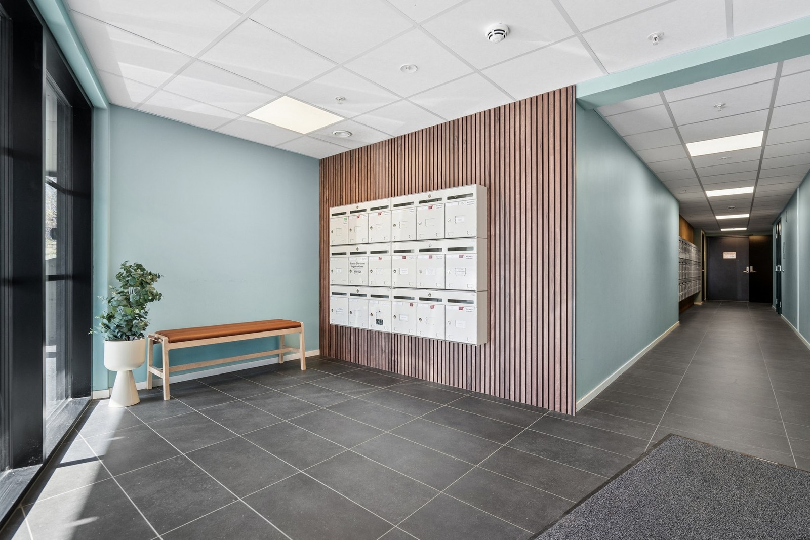 Felles inngangsparti med postkasser og sittebenk, som fremstår som moderne og innbydende. Galleribilde