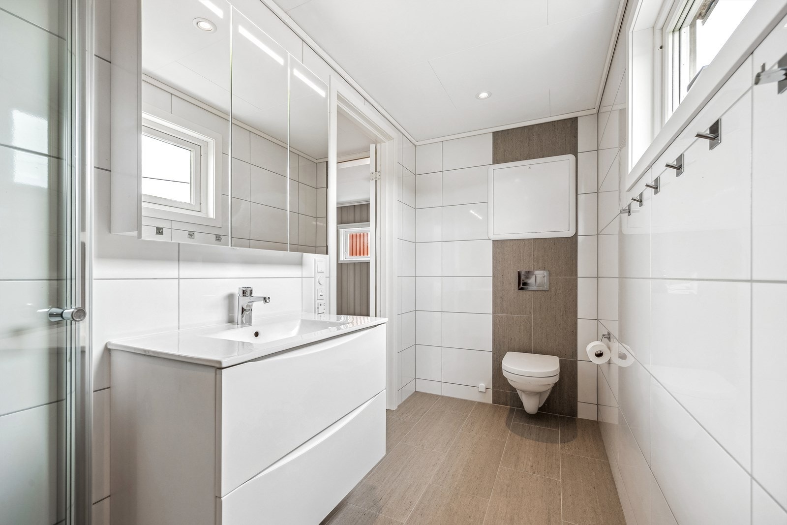 Badet har moderne innredning med servant, speilskap med belysning, vegghengt toalett, dusjhjørne og downlights i himling samt gulvvarme. Galleribilde
