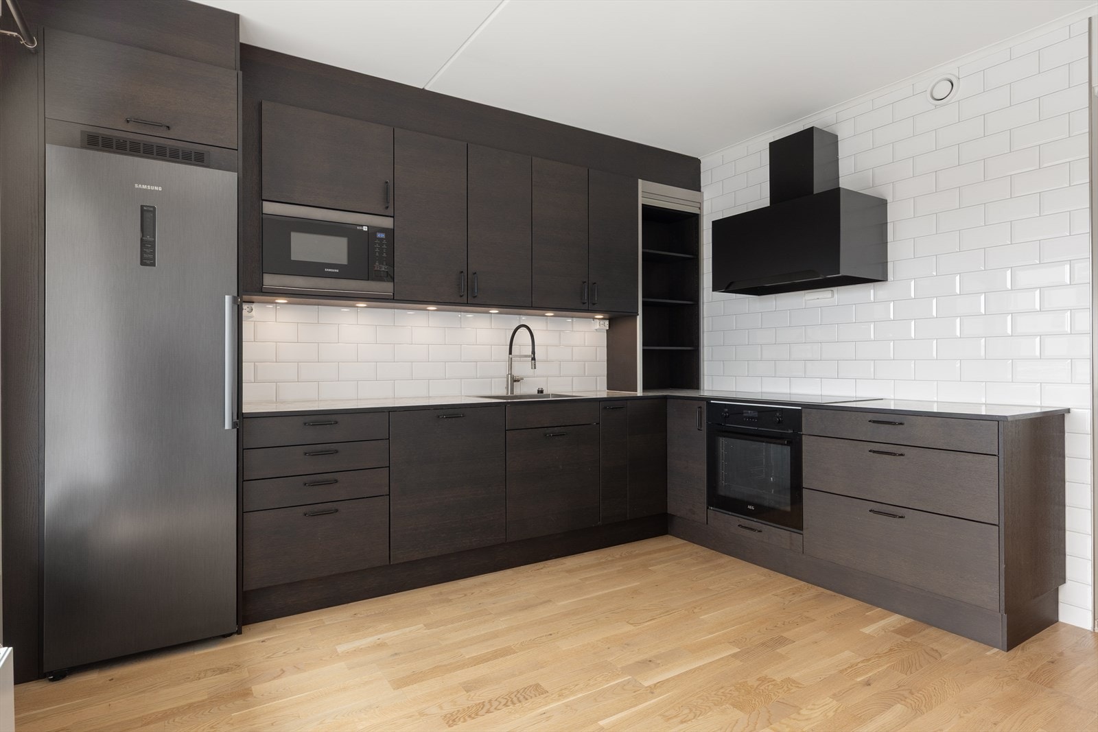 Innredning med glatte fronter, laminatbenkeplate og utstyr som induksjonstopp, stekeovn og oppvaskmaskin. Galleribilde