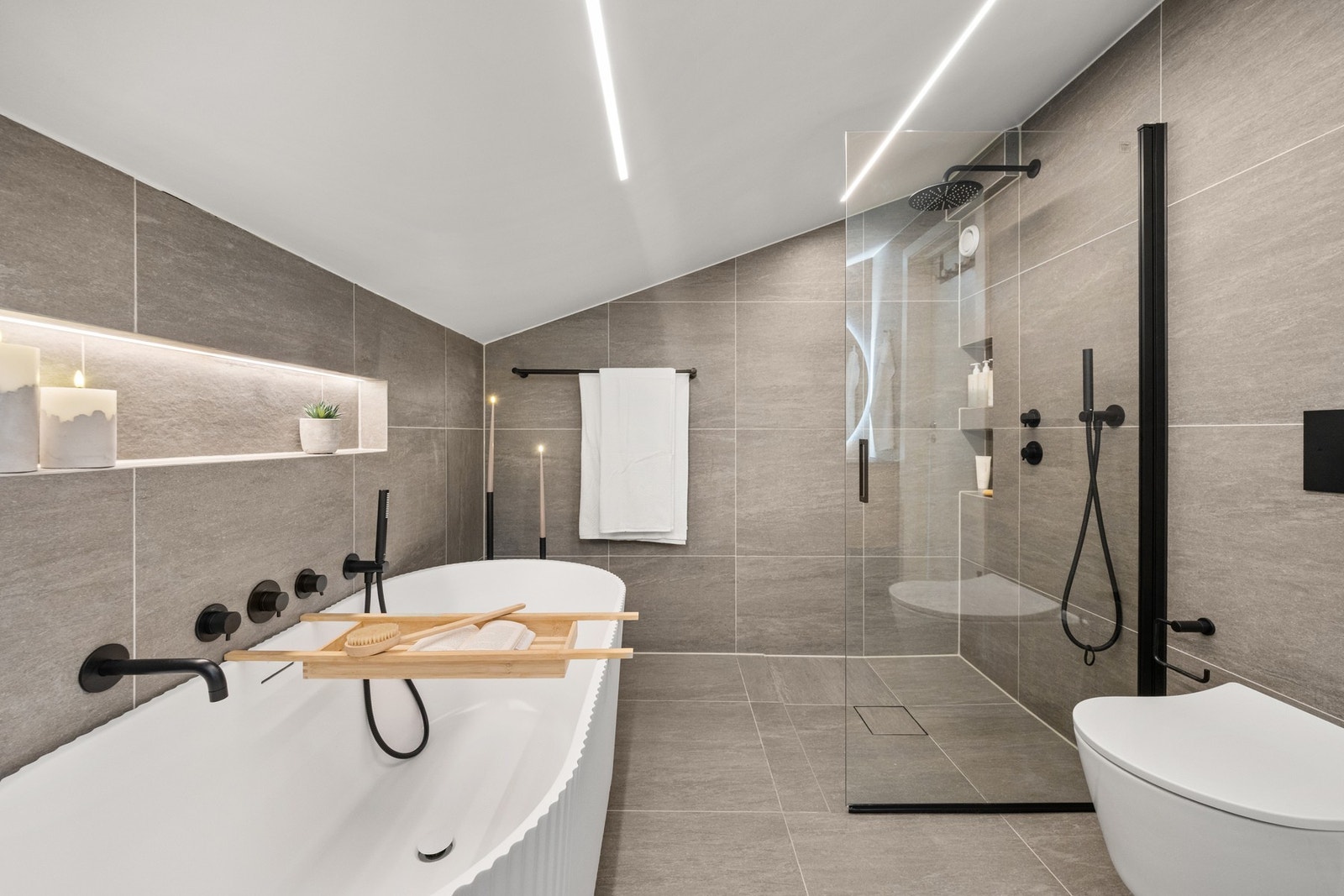 Badet er utstyrt med vegghengt toalett, badekar og dusjhjørne med innfellbare glassdør, en plassbesparende og stilren løsning som gir et luftig uttrykk. Galleribilde