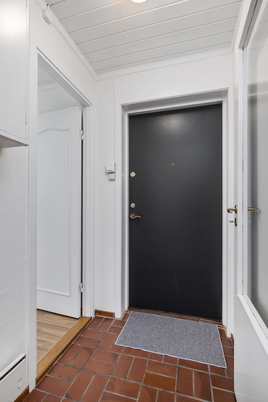 Entréen har sikringsskapet lett tilgjengelig og en dør med glassfelt som leder inn til stuen. Galleribilde