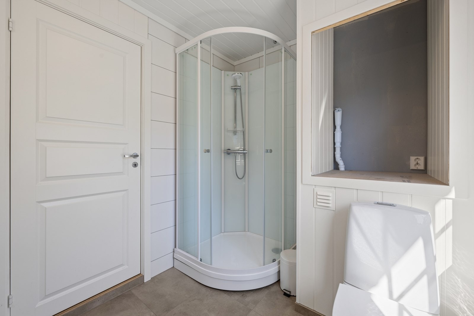 Badet er praktisk innredet med dusjkabinett og en plassbygget nisje med opplegg for vaskemaskin over toalettet. Vannledninger er i rør-i-rør-system. Galleribilde