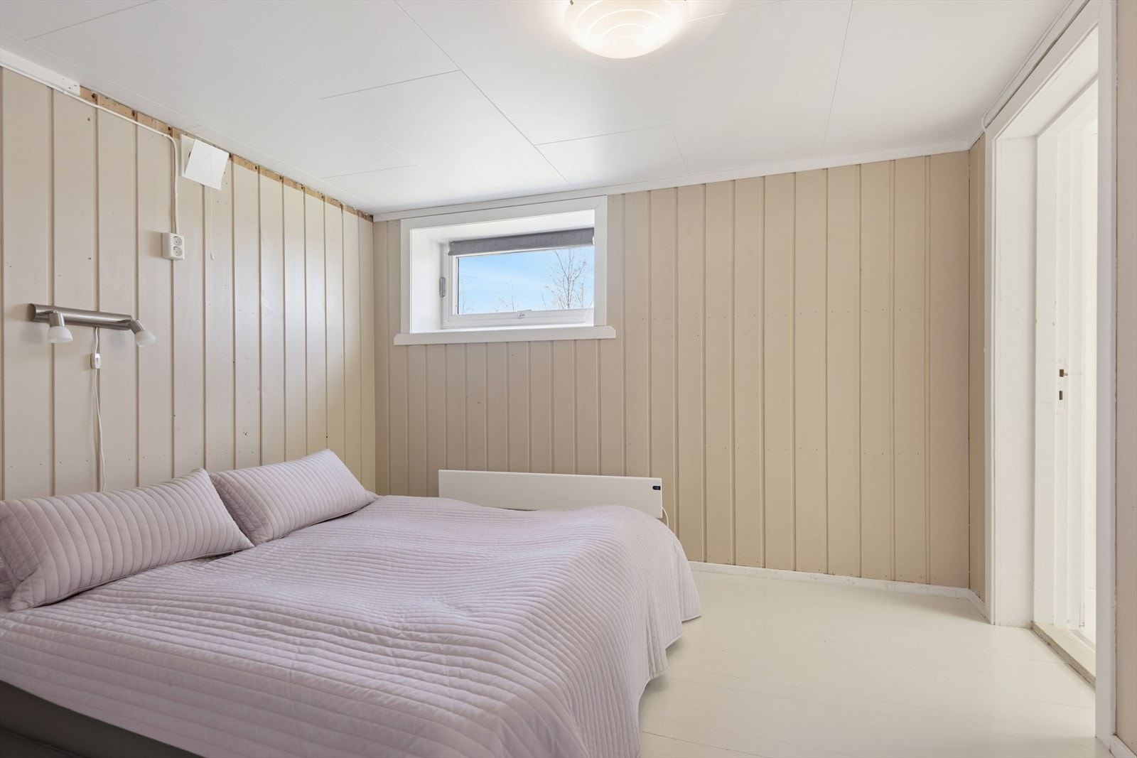 Lyst rom i kjeller med panel på veggene og malt tregulv. Galleribilde