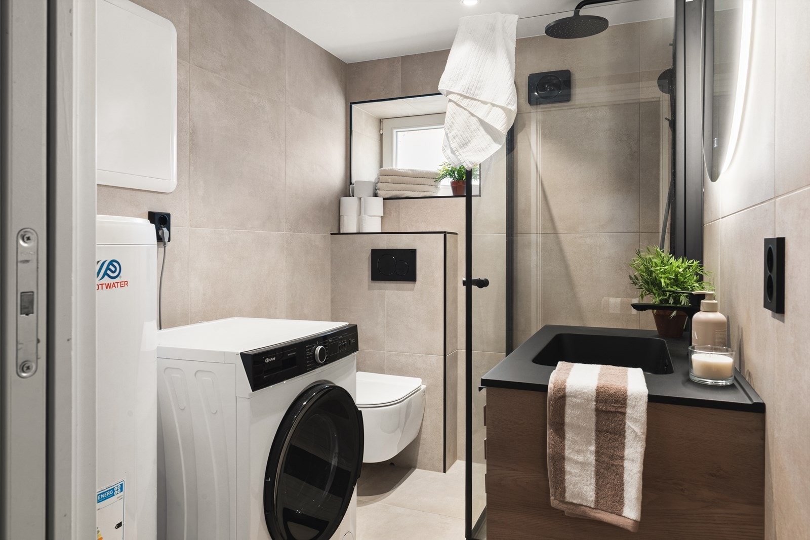 Badet er utstyrt med vegghengt toalett, dusj m/glassvegger, baderomsinnredning og opplegg for vaskemaskin Galleribilde