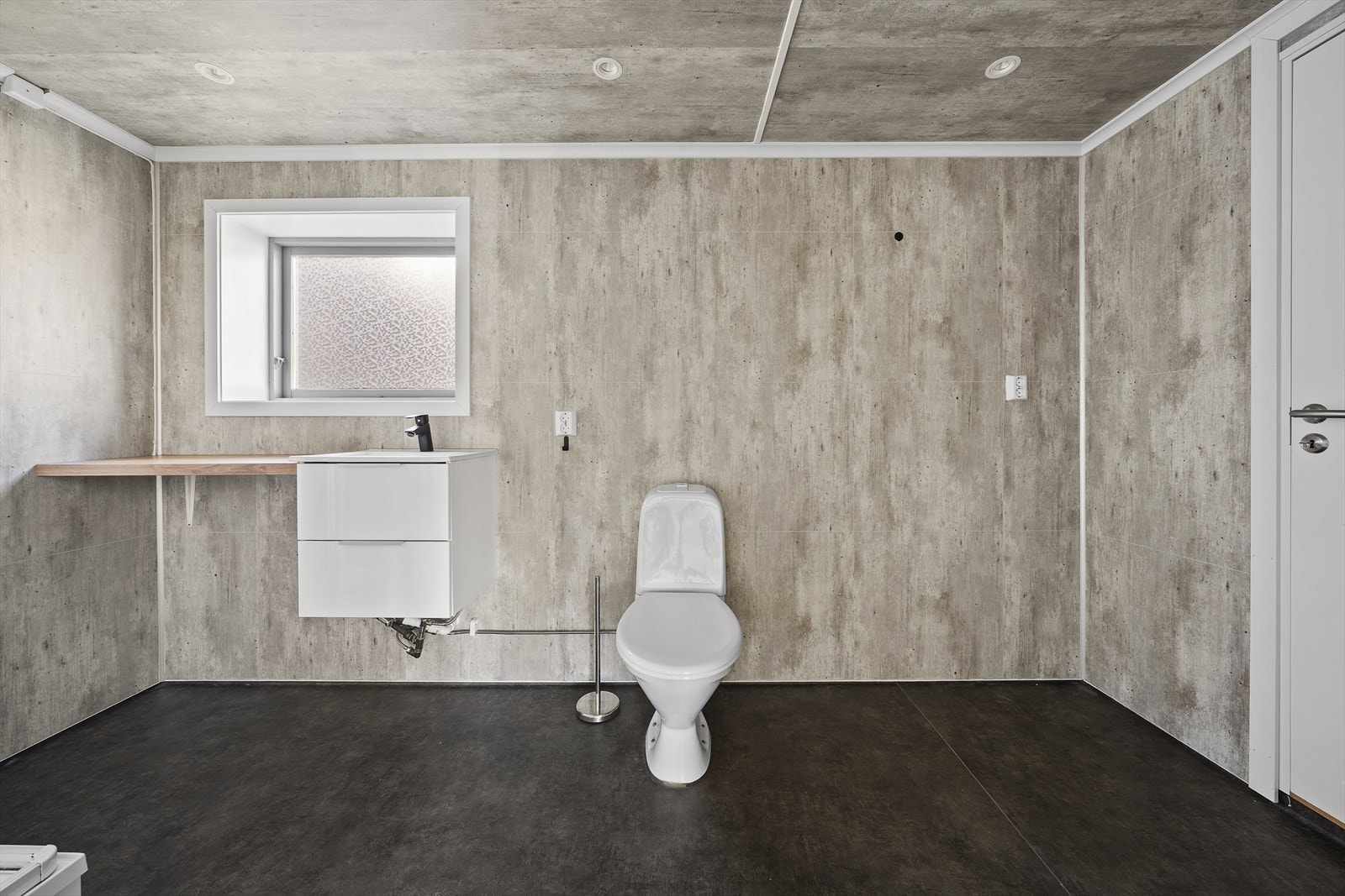 Badet har belegg på gulv og baderomsplater på vegger. Baderommet er utstyrt med servant over skuffeinnredning, dusjkabinett og toalett Galleribilde