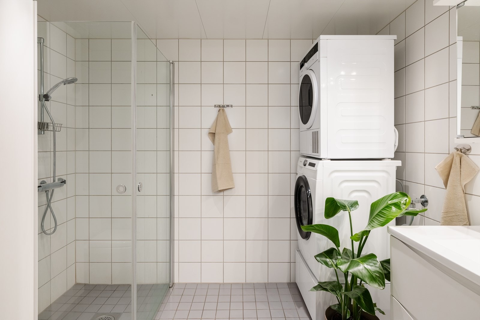 Flislagt bad med varmekabler i gulvet, dusjhjørne og opplegg for vaskemaskin. Galleribilde