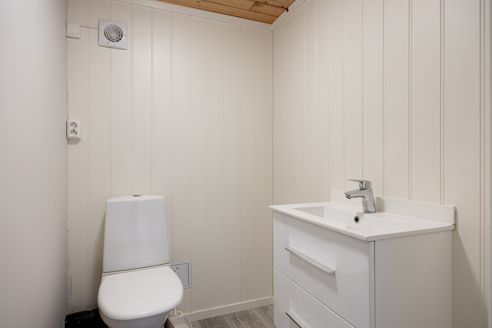 I kjelleren er wc-rommet innredet med laminatgulv, gulvmontert toalett og en heldekkende servant med hvite skuffer. Galleribilde