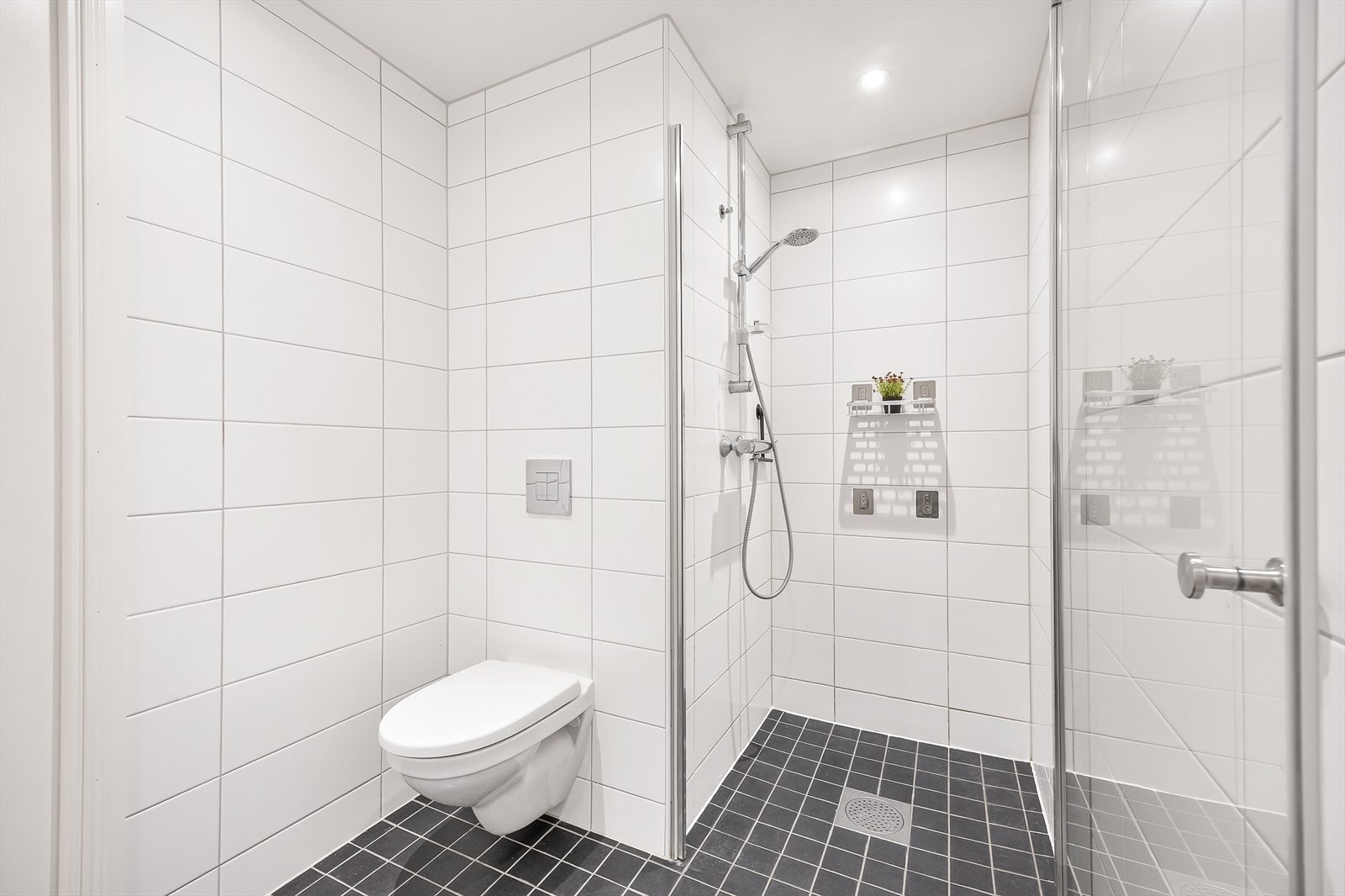 Badet er innredet med vegghengt toalett, servant i baderomsinnrending, dusjhjørne og opplegg for vaskemaskin. Galleribilde